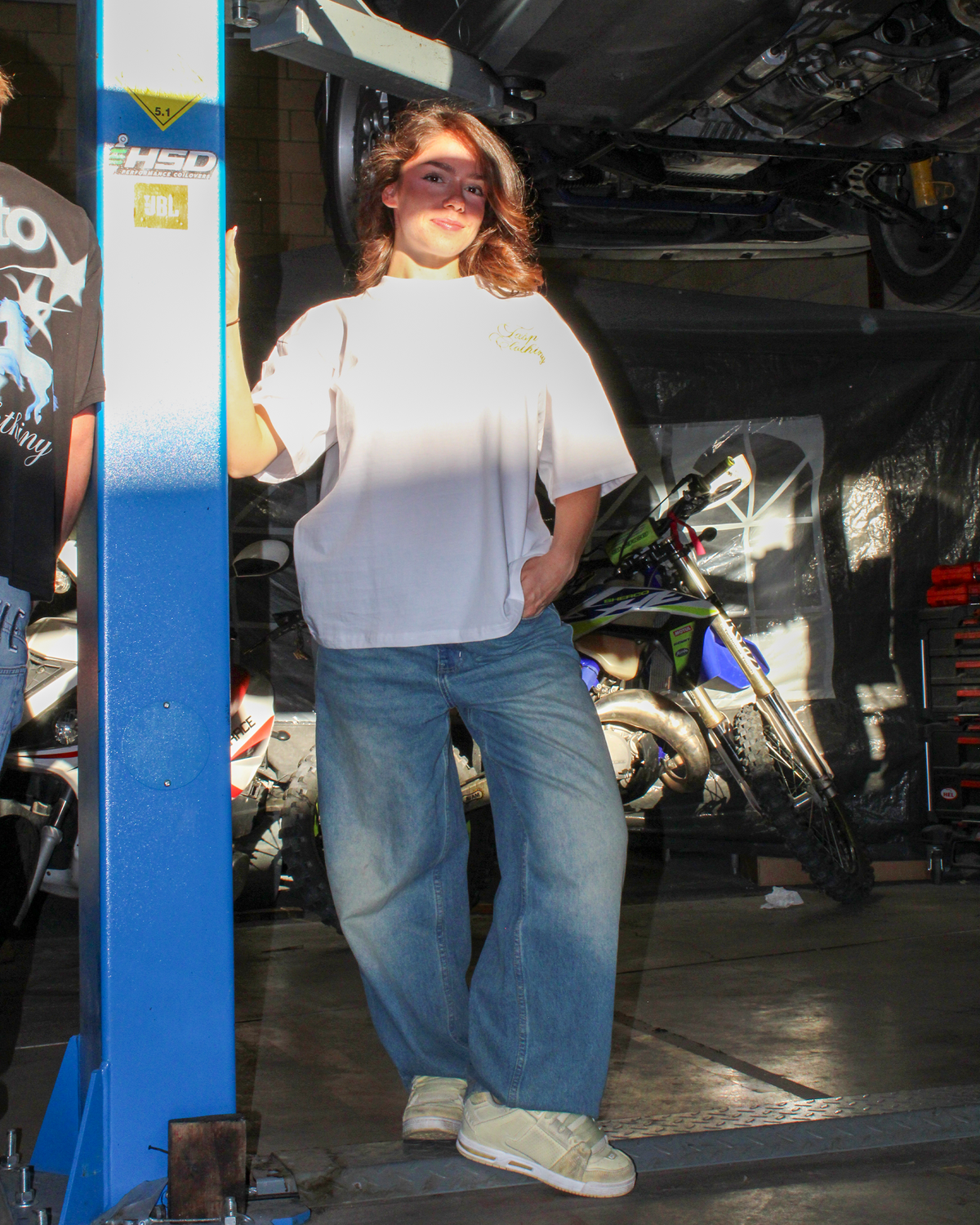 Modelo con camiseta oversize blanca ANGEL de TASP Clothing y vaqueros anchos en un taller, look streetwear